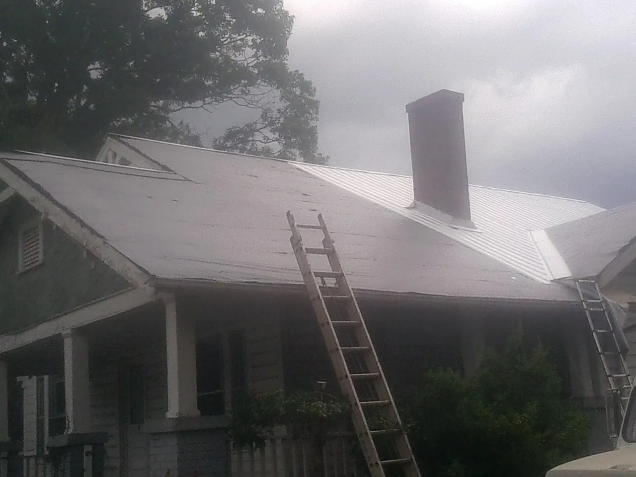 Ladders against a metal roof on an older home with a brick chimney in Montezuma